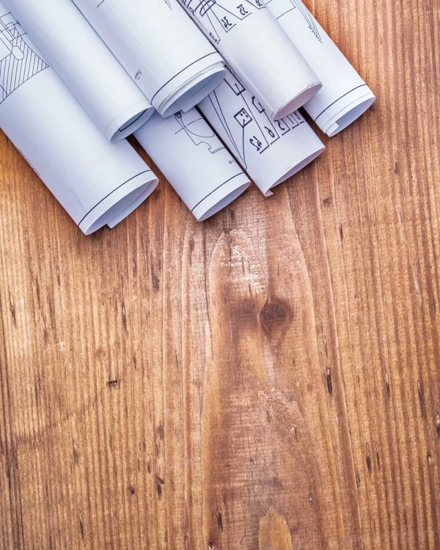 Rolled construction drawings resting on a warm wooden board