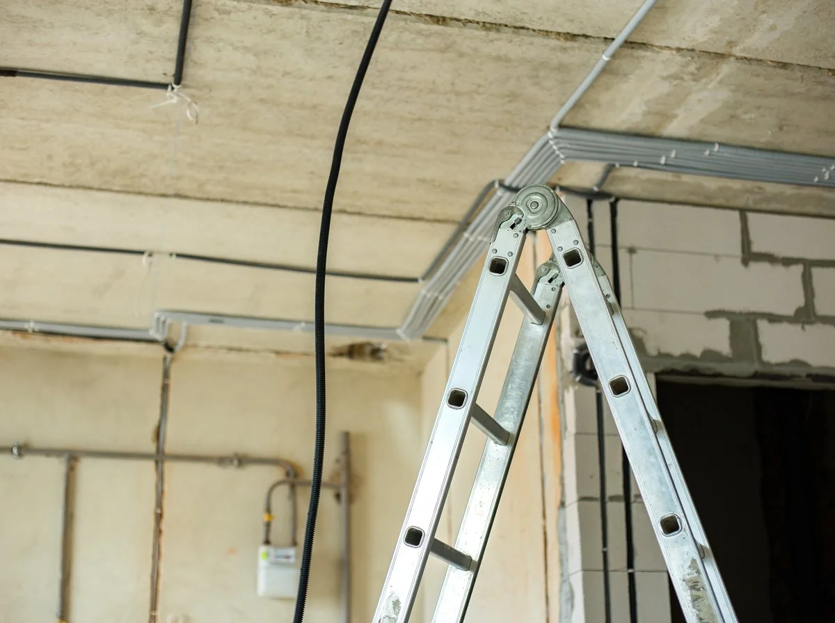Stepladder standing against a bare concrete ceiling with surface conduit
