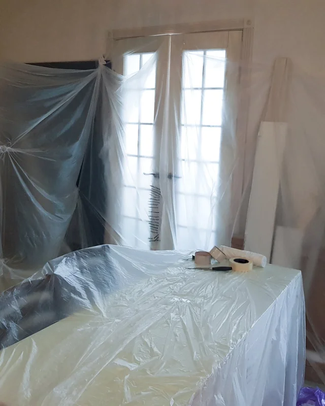 Furniture and a doorway sheeted in plastic inside an occupied room