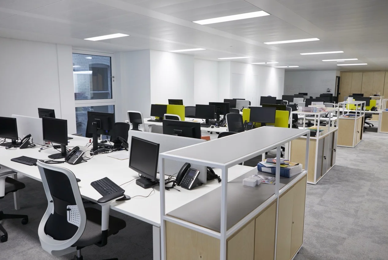 Open plan business office with desks and monitors, empty, in early evening light