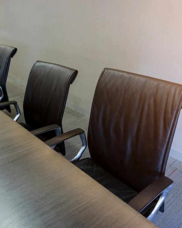 Row of leather meeting chairs receding along a boardroom table
