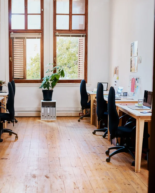 Small office of timber desks by sash windows, nobody at them