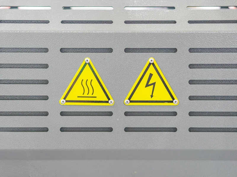 Hot surface and high voltage warning labels riveted to a ventilated grey enclosure