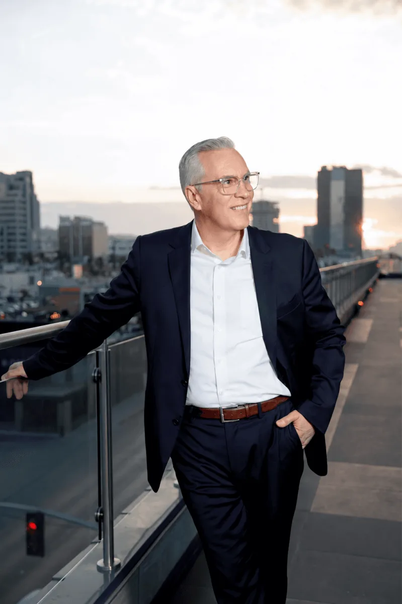 Rosella broker in a suit leaning on a rooftop railing against a city backdrop at dusk