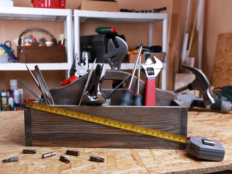 Hand tools and a tape measure in an open tool tray on a bench