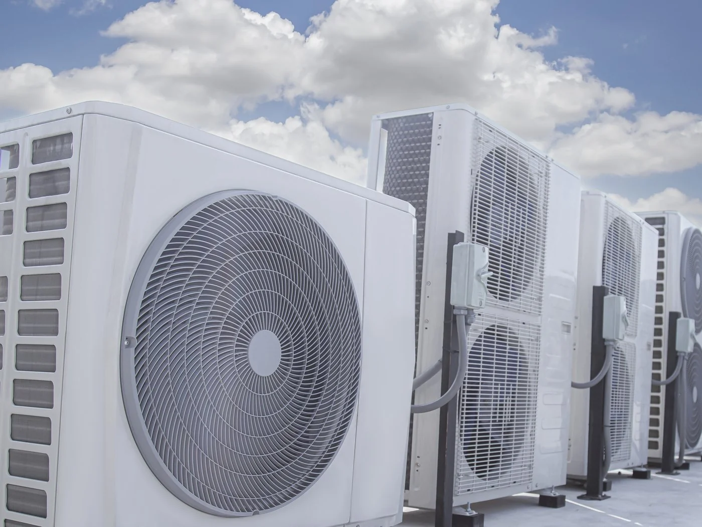 Row of outdoor air conditioning condenser units on a flat roof against a clear sky