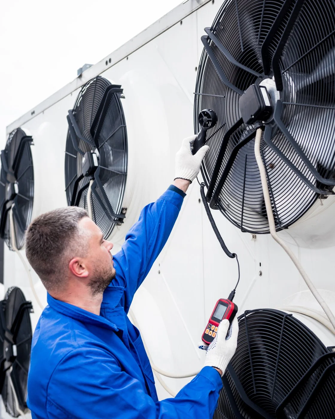 Technician testing the axial fans of a commercial condensing unit with an anemometer