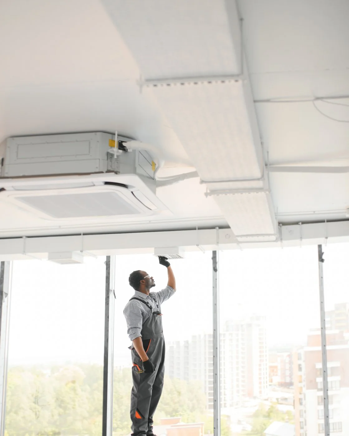 Technician on a ladder installing rectangular ductwork in an unfinished commercial interior