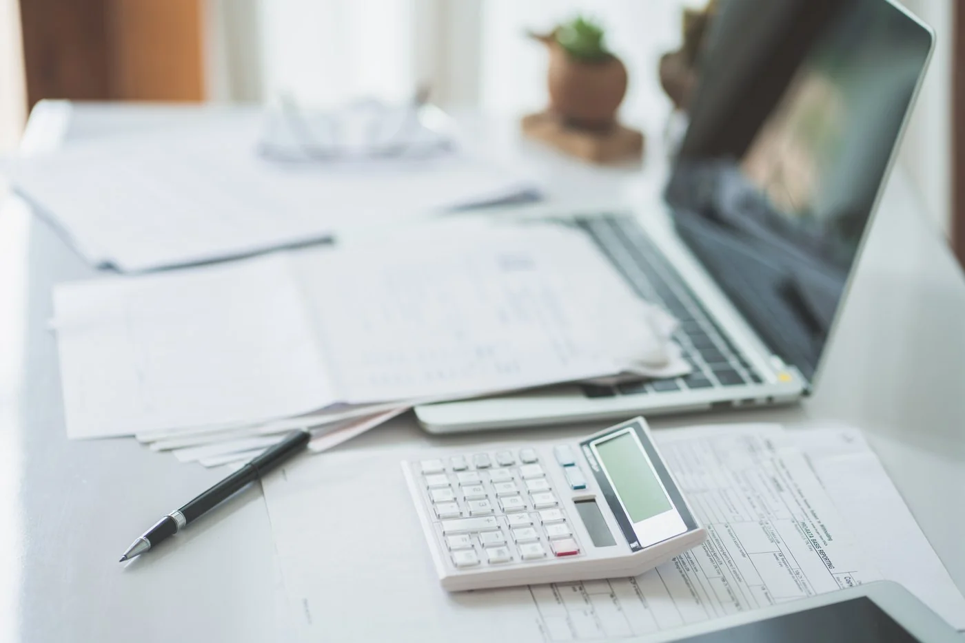 Loss runs and a payroll schedule spread on a desk beside a calculator and laptop