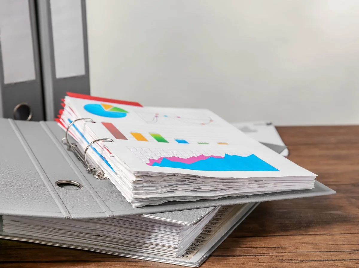 Ring binders and a stack of printed reports on a timber desk