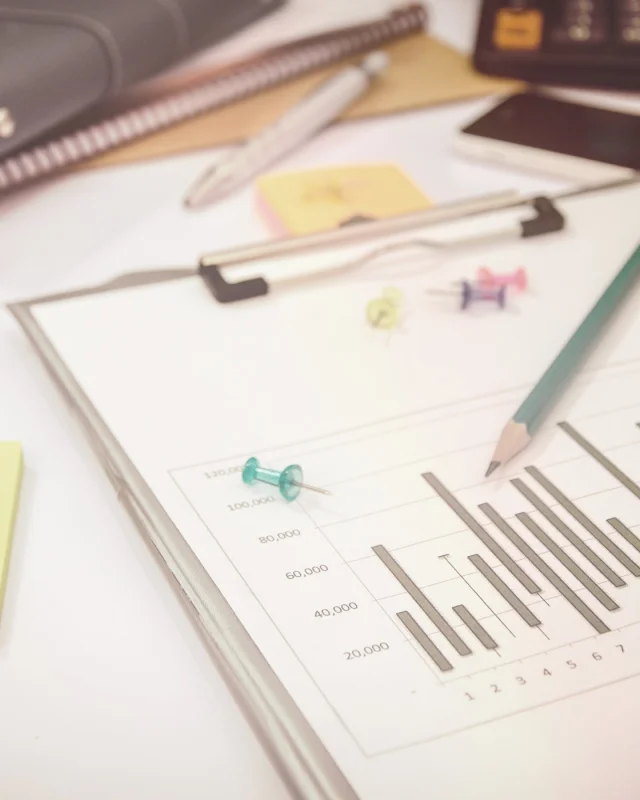 Clipboard carrying a printed bar chart, with a pencil and reading glasses
