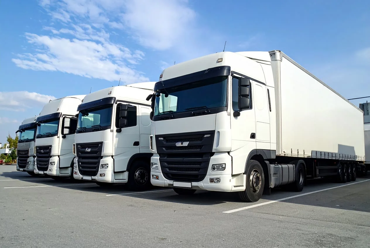 Row of white tractor units parked in line at a depot, one coupled to a curtainside trailer