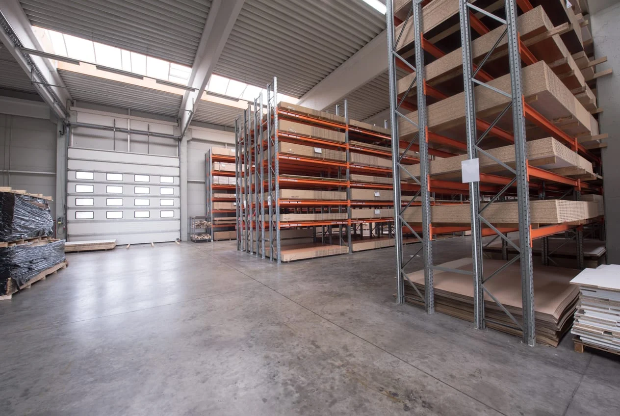 Empty workshop interior with steel racking, stacked board and a roller door