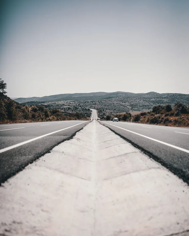 Empty two lane road running straight to a low ridge under a pale sky